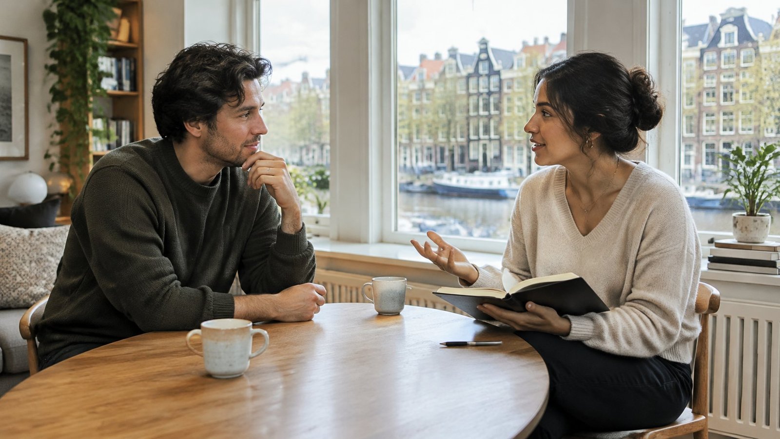 Two people talking over coffee at a table in a bright Amsterdam apartment